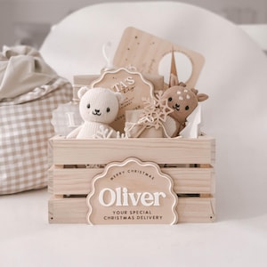 May include: A wooden crate filled with Christmas-themed gifts. The crate features a sign that says "Merry Christmas Oliver, Your Special Christmas Delivery." Inside are a teddy bear, a deer, and other decorative items.