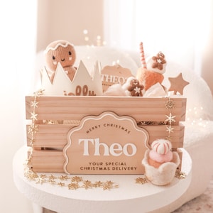 May include: A wooden crate filled with Christmas-themed plush toys and decorations. The crate features a sign that reads "Merry Christmas Theo, Your Special Christmas Delivery." Includes a gingerbread man, star, and cupcake.