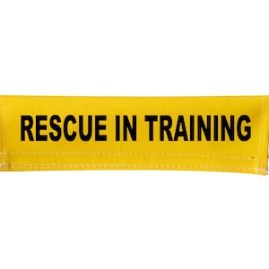 May include: Yellow fabric strap with black text that reads "RESCUE IN TRAINING".