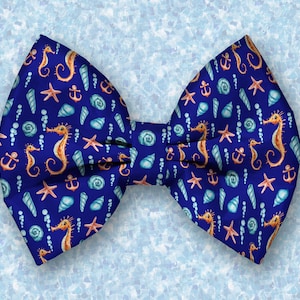 May include: A blue bow tie featuring a nautical design. The bow tie is patterned with seahorses, seashells, anchors, and starfish.