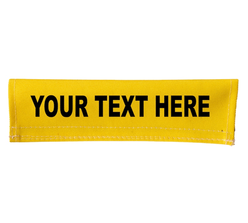 Op de afbeelding: Een gele stoffen band met zwarte stiksels en de tekst "YOUR TEXT HERE" in het zwart gedrukt.