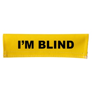 Peut inclure: Une sangle en tissu jaune avec le texte "I'M BLIND" imprimé en noir.