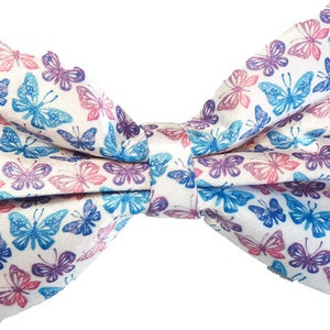 May include: A white bow tie patterned with blue, purple, and pink butterflies. The bow tie is tied in a classic style, suitable for formal or semi-formal occasions. The butterflies are in a repeating pattern.