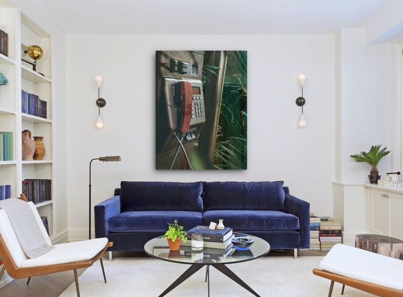 May include: A vintage, silver payphone with a red receiver hanging off the hook. The phone is mounted on a wall with green foliage behind it.