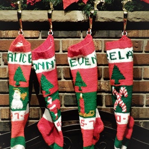 May include: Four red and green knitted stockings with white trim hanging on a fireplace mantle. The stockings are decorated with different designs, including a snowman, a Santa Claus, a candle, and candy canes. The stockings are labeled "Alice", "Tommy", "Even", and "Bella".