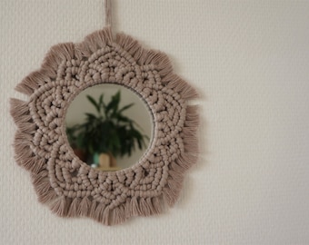 Peut inclure: Un miroir rond avec un cadre en macramé de couleur brun clair. Le miroir est suspendu à un mur blanc.
