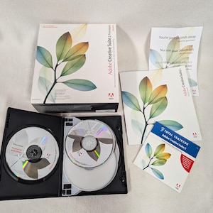 May include: A two-disc set of Adobe Creative Suite 2 software in a black case with a green and white leaf design on the cover. The software is for educational purposes and includes a total training guide.