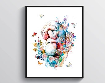 Op de afbeelding: Aquarel kunstafdruk van een baby in foetushouding, omringd door kleurrijke bloemen en vlinders. Het kunstwerk toont een levendige mix van blauw, roze en geel, tegen een witte achtergrond, ingelijst in een zwarte lijst.