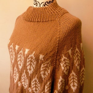May include: A tan-colored knitted sweater with a high, ribbed collar and white geometric patterns. The sweater features a close-up view, showcasing the texture and design of the knitwear. The pattern is repeated across the chest and sleeves.