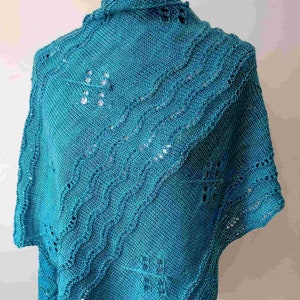 May include: A teal blue knitted shawl with a lacy pattern. The shawl is draped over a mannequin.