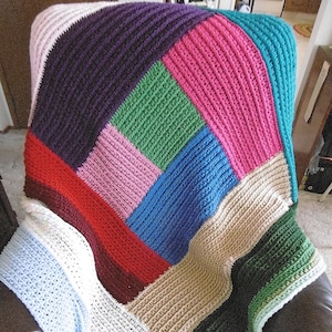 May include: A crocheted blanket with a patchwork design in shades of blue, green, pink, red, white, and brown.
