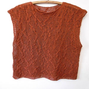 May include: A rust-colored sleeveless knitted top with a loose, open weave.