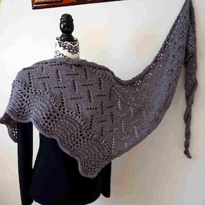 Puede incluir: Un chal de punto gris con un patrón de encaje. El chal está drapeado sobre un maniquí negro.