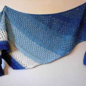 May include: A knitted shawl in shades of blue and white, with a gradient effect. The shawl features openwork and a textured pattern. The edges are finished with a darker blue border. This handmade accessory is perfect for adding a touch of elegance.