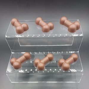 May include: Six brown, bone-shaped treats are arranged on a clear, tiered display. Each treat has a rounded shape with three circular ends and a rectangular center with three etched lines. The treats are evenly spaced on the display.