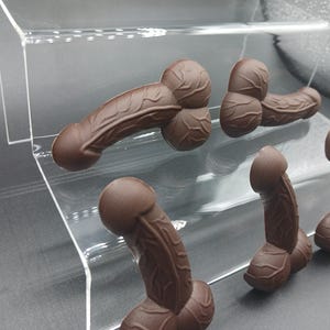 Op de afbeelding: Vijf gegoten chocolade figuren in verschillende vormen en maten op een transparante acryl displaystandaard.
