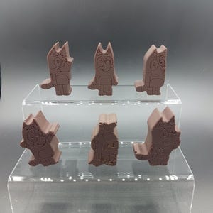 Op de afbeelding: Zes bruine cartoonhondfiguren worden tentoongesteld op een heldere, gelaagde plank. De beeldjes hebben de vorm van een hond met grote oren en een staart. De figuren kijken allemaal in verschillende richtingen.