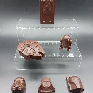 Könnte beinhalten: Eine Sammlung von Star Wars-Charakteren aus Schokolade, darunter Darth Vader, Boba Fett, ein Sturmtruppler, R2-D2 und Han Solo, eingefroren in Carbonit. Die Schokoladenfiguren werden auf einem transparenten, mehrstufigen Acryl-Ständer präsentiert.