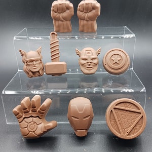 Puede incluir: Un conjunto de nueve figuras de chocolate con personajes y símbolos del universo Marvel. Las figuras son marrones e incluyen a Thor, Capitán América, Iron Man, Hulk y el logotipo de los Vengadores.