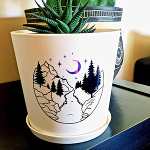 Op de afbeelding: Witte keramische pot met een zwart-witte illustratie van een bergketen, een rivier en een halve maan met sterren. De pot heeft een witte schotel.