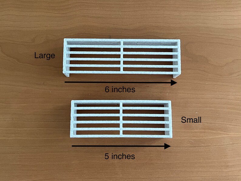 K&ouml;nnte beinhalten: Zwei wei&szlig;e, rechteckige L&uuml;ftungsgitter, eines mit der Aufschrift "Large" und einer Gr&ouml;&szlig;e von 15 cm, das andere mit der Aufschrift "Small" und einer Gr&ouml;&szlig;e von 13 cm. Beide haben horizontale Lamellen und sind auf einer braunen Oberfl&auml;che dargestellt.