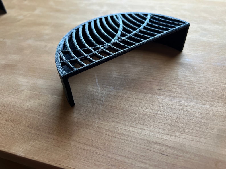 May include: A black, 3D printed, semi-circular shelf with a geometric design. The shelf is made of a sturdy, durable material and has a modern, minimalist aesthetic.