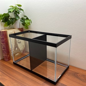 Peut inclure: Un aquarium en verre avec un cadre noir et un s&eacute;parateur, pos&eacute; sur une surface en bois.
