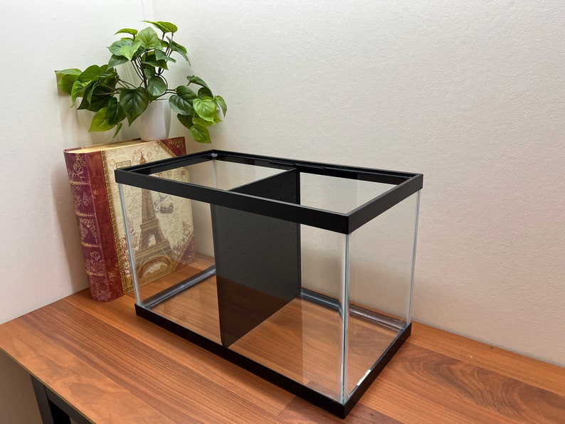 Peut inclure: Un aquarium en verre avec un cadre noir et un s&eacute;parateur, pos&eacute; sur une surface en bois.