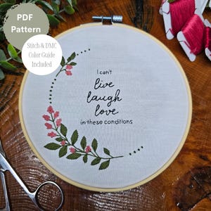 May include: Embroidered hoop art featuring a floral design and the text "I can't live laugh love in these conditions".