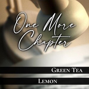 Puede incluir: Una etiqueta de vela con el texto One More Chapter, Green Tea, Lemon, Exhaustion, Hand Poured, 3 oz y 100% Soy Wax. El fondo muestra una l&aacute;mpara de escritorio borrosa y un libro abierto, con un logotipo que presenta la letra M.