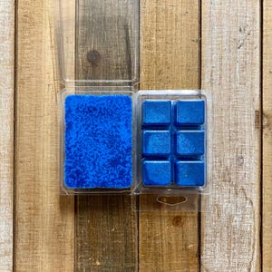 May include: Two clear plastic containers of blue wax melts. One container holds a single large melt, the other holds six smaller square melts.