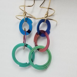 Op de afbeelding: Gouden creolen met meerdere regenboogkleurige ringen in blauw, groen en rood. De oorbellen zijn gemaakt door "Harry Mason Designer Jewelry, California".