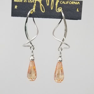 May include: A pair of silver dangle earrings with a twisted wire design and peach-colored teardrop crystals. The earrings are on a card that says "Harry Mason, California".