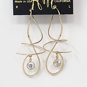 May include: Gold dangle earrings with a single clear crystal dangling from each earring. The earrings are made of twisted wire and have a simple, elegant design. The earrings are on a black card with the text "HARRY MASON" and "CALIFORNIA" printed on it.