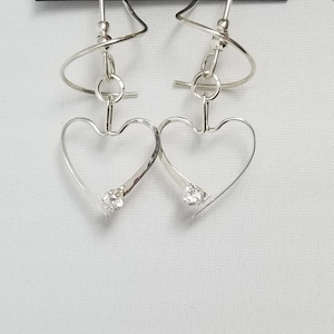 May include: Silver heart shaped earrings with a small clear crystal in each heart. The earrings are on a card that says "Harry Mason Designer Jewelry, Made in USA, California".
