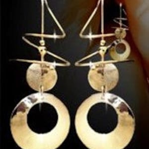May include: Gold-toned geometric earrings with a layered design. Each earring features a large circular hoop at the bottom, a smaller disc, and a triangular shape at the top. The earrings have a shiny finish and a modern aesthetic.