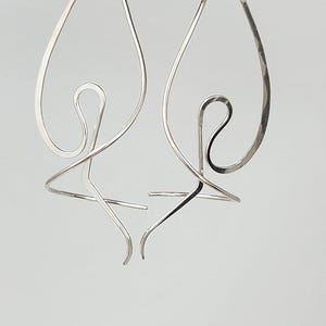 May include: A pair of silver hoop earrings with a unique, abstract design. The earrings are made of hammered metal and have a slightly textured finish.