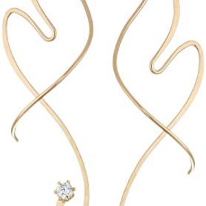 May include: A pair of gold-toned earrings with a delicate, abstract design. Each earring features a single clear crystal at the bottom.