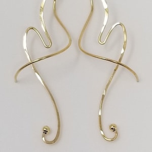 May include: A pair of gold-toned, abstract, wire earrings with a small ball at the end of each earring.