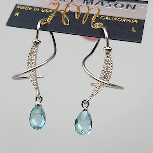 May include: A pair of silver dangle earrings with a teardrop-shaped blue gemstone hanging from each. The earrings feature a curved, twisted design with small clear stones.