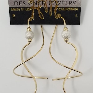 May include: Gold tone earrings with a twisted wire design and a small, textured silver ball at the end of each earring.