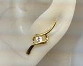 May include: Gold ear cuff with a single clear stone set in a curved design.