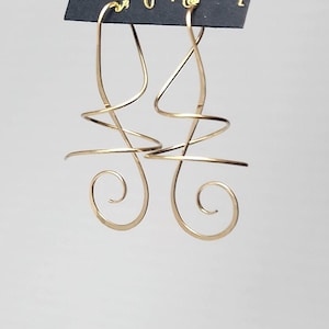 May include: Gold-toned, abstract swirl earrings. The earrings feature a looping design with spiral and linear elements. The earrings are displayed on a black card with the text "HARRY MASON" and "Made in USA".