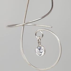 Op de afbeelding: Zilveren oorhangers met een enkel helder kristal dat aan een gebogen draad hangt.