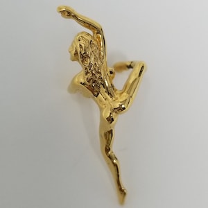 May include: A gold-colored figurine of a woman in a stylized pose. The figurine is detailed and has a smooth, polished finish.