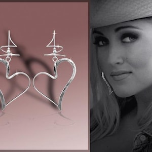 May include: A pair of silver heart-shaped earrings with a delicate, abstract design. The earrings are dangling and have a hammered texture.