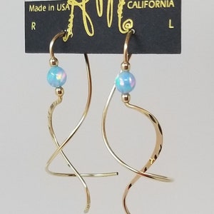 May include: Gold hoop earrings with a blue opal bead on each earring. The earrings are displayed on a black card with the text "HARRY MASON DESIGNER JEWELRY CALIFORNIA" printed on it.