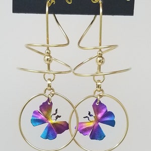 Op de afbeelding: Gouden oorbellen met een spiraalvormig ontwerp en een kleurrijke vlinderbedel. De oorbellen zijn gemaakt door Harry Mason Designer Jewelry, Californië.