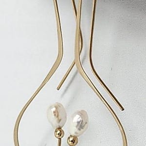 May include: A pair of gold-tone earrings with a unique heart-shaped design. Each earring features a single white pearl.