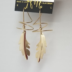 May include: Gold tone earrings with a feather design and a spiral wire detail. The earrings are labeled "Harry Mason, California".
